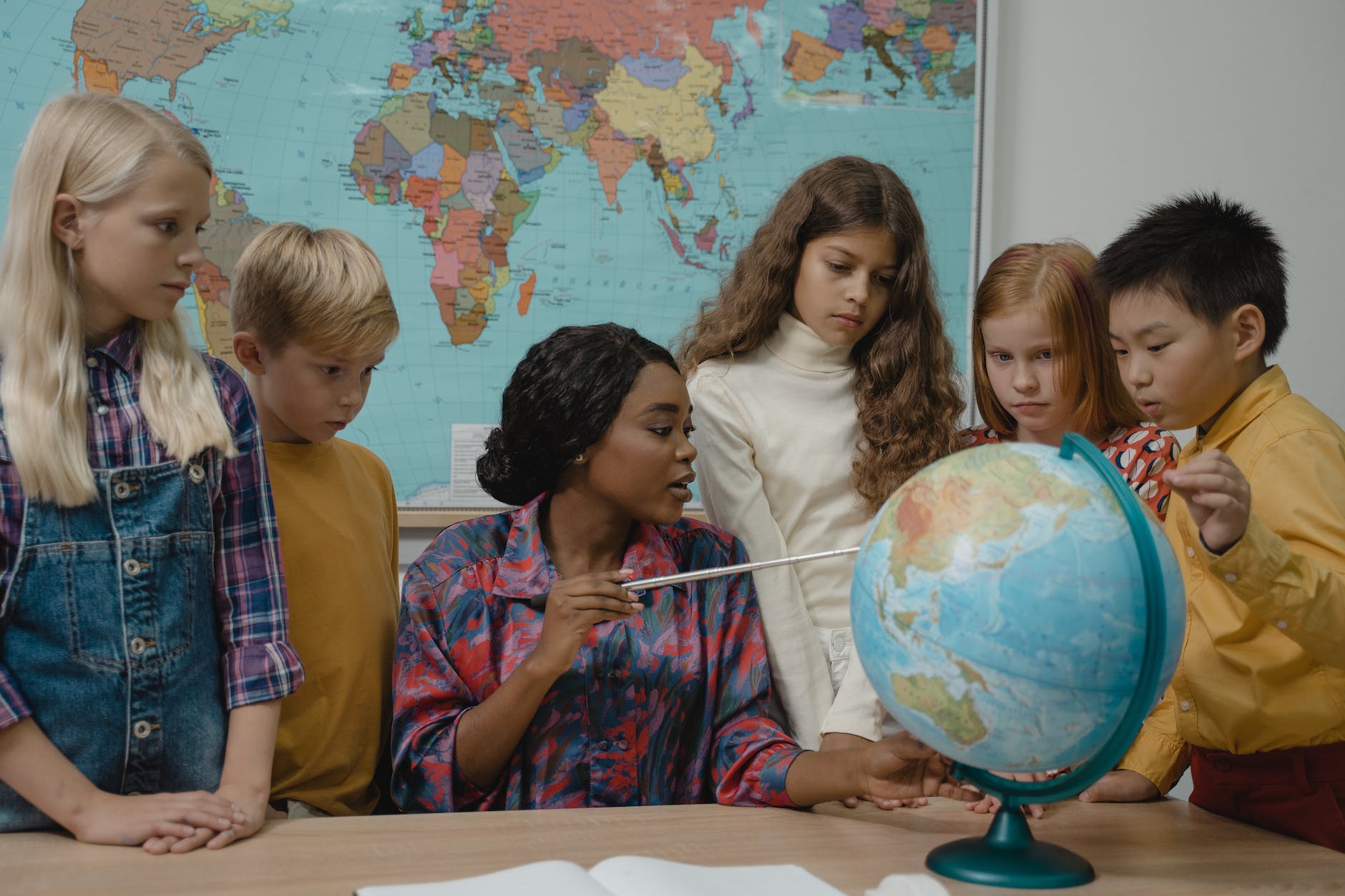 teacher teaching students about geography using a globe, online teaching degree, online courses for teachers 